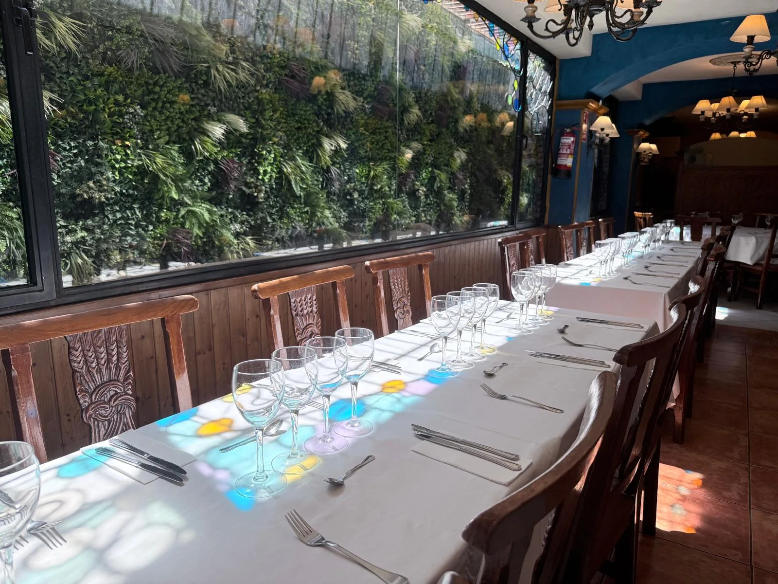 Mesa alargada con copas junto a un ventanal con vegetación al otro lado.