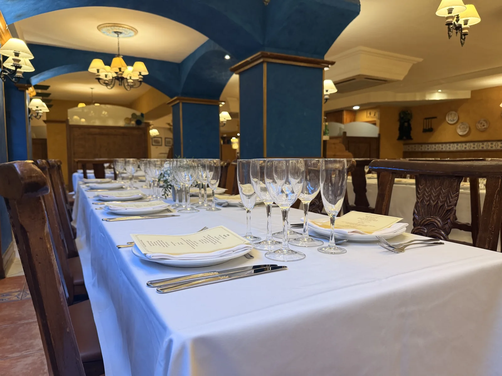 Detalle de una mesa preparada con copas, platos y manteles blancos junto a columnas azules.